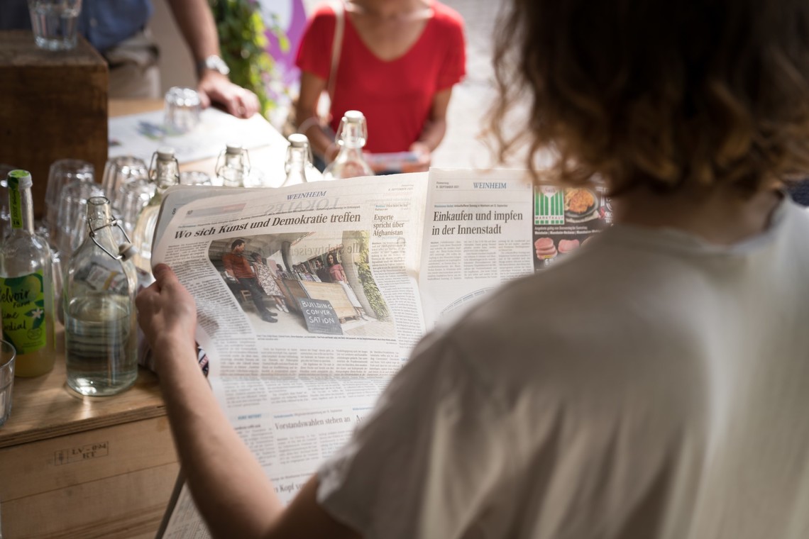 Einem Menschen von hinten über die Schulter fotografiert, er liest einen Zeitungsartikel mit dem Titel "Wo sich Kunst und Demokratie treffen" | © Gunnar Fuchs