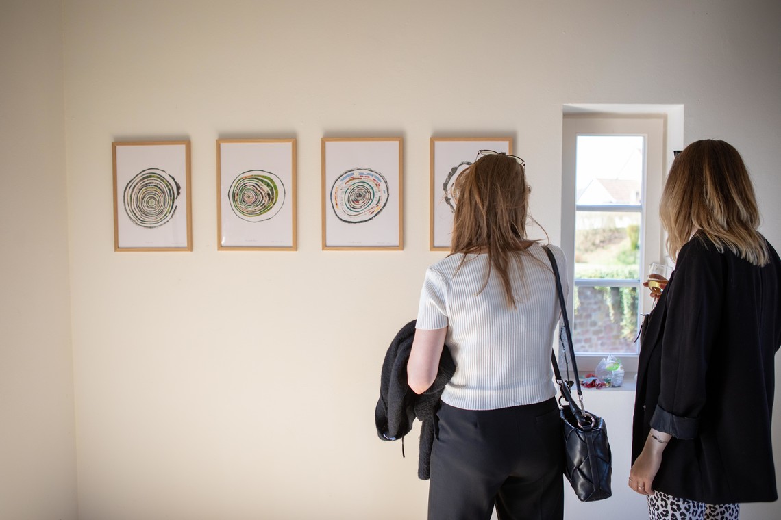 Zwei Personen betrachten vier an die Wand eines Ateliers gehängte Collagen | © Elisa Berdica