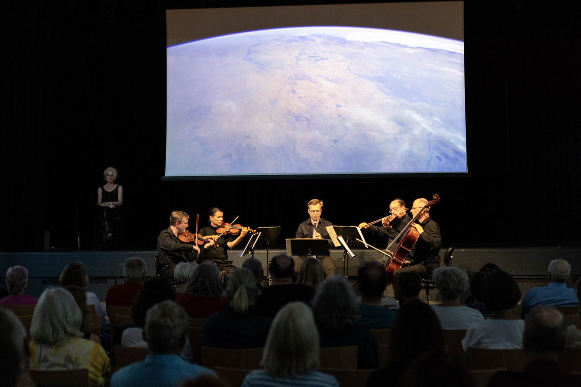 Ein Kammerorchester spielt vor einer Leinwand, die Bilder des Planeten Erde zeigt | © Arthur Bauer