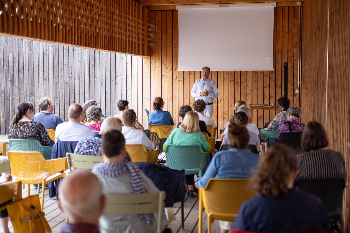 Eine Gruppe Menschen auf Stühlen hört einem Vortragenden zu | © Arthur Bauer