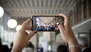 Parlamentarischer Abend der Metropolregion Rhein-Neckar | © VRRN/Schwerdt Smartphone in den Händen nimmt ein Foto der Bühne auf. Mehrere Menschen unscharf im Hintergrund | © VRRN/Schwerdt