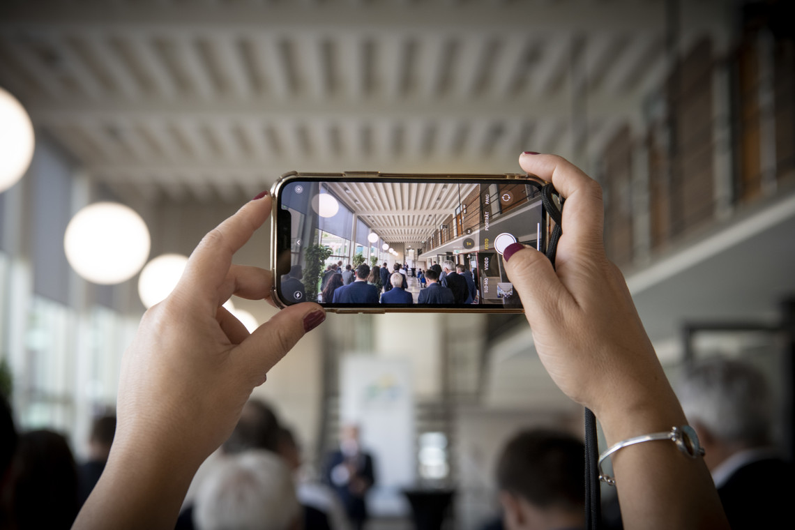 Smartphone in den Händen nimmt ein Foto der Bühne auf. Mehrere Menschen unscharf im Hintergrund | © VRRN/Schwerdt