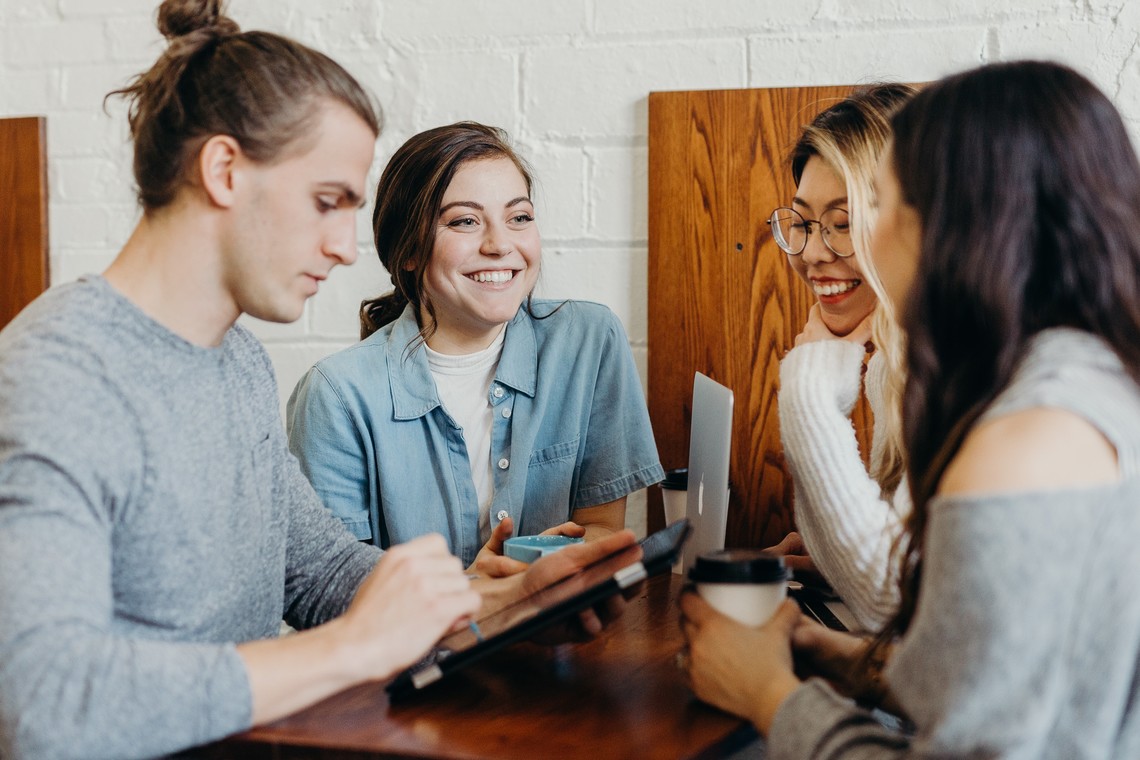 Personen sitzen gemeinsam an einem Tisch, arbeiten und unterhalten sich | © Unsplash (frei)