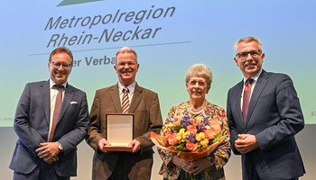 v.l.n.r. Verbandsdirektor Ralph Schlusche, Manfred Schwarz, Veronika Schwartz, Verbandsvorsitzender Stefan Dallinger | © VRRN / Schwerdt Drei Männer und eine Frau auf einem Podium. Einer hält eine Plakette, die Frau einen Blumenstrauß in der Hand | © VRRN / Schwerdt