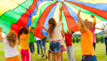 Eine Gruppe Kinder spielt auf einer Wiese mit einer bunten Plane | © Shutterstock Standard Lizenz