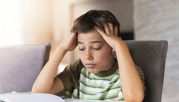 SchuleZuhause | © iStock/PIKSEL Ein Junge sitzend, stützt die Ellenbogen auf den Tisch und hat die Hände im Gesicht und schaut überfordert | © iStock/PIKSEL