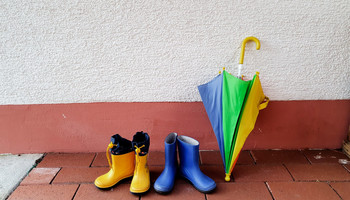 Das Bild zeigt 2 Kindergummistiefel und einen bunten Regenschirm die an der Wand stehen | © VRRN/Le